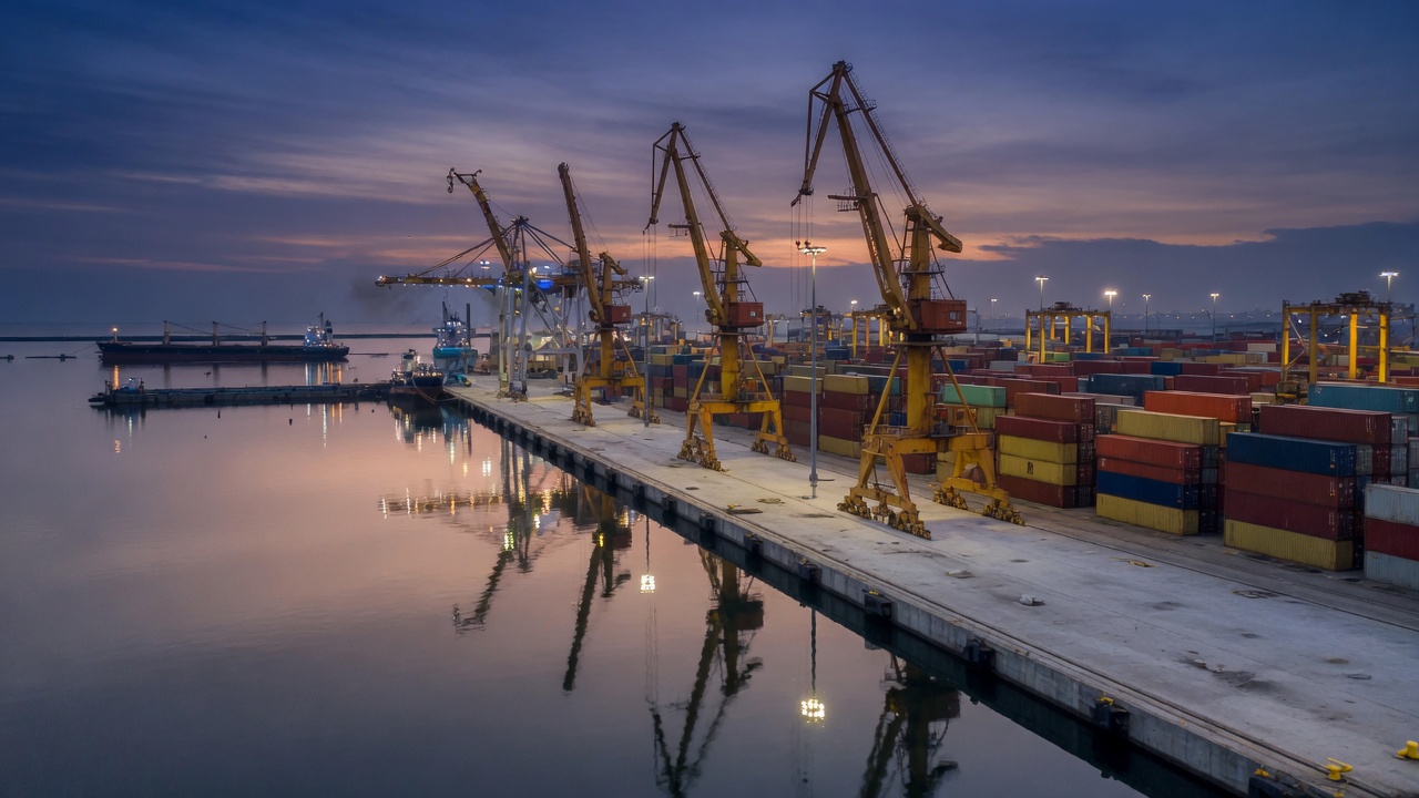 Container cranes along a still harbor at dusk